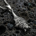 Load image into Gallery viewer, Sterling silver hanging bat pendant necklace with an oxidized finish resting on textured volcanic rock, captured in a close-up premium studio composition.
