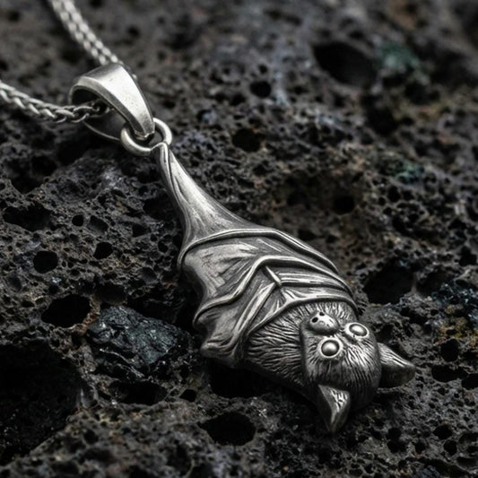 Sterling silver hanging bat pendant necklace with an oxidized finish resting on textured volcanic rock, captured in a close-up premium studio composition.