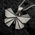 Load image into Gallery viewer, Sterling silver origami butterfly pendant necklace with an oxidized finish resting on textured volcanic rock, captured in a close-up premium studio composition.
