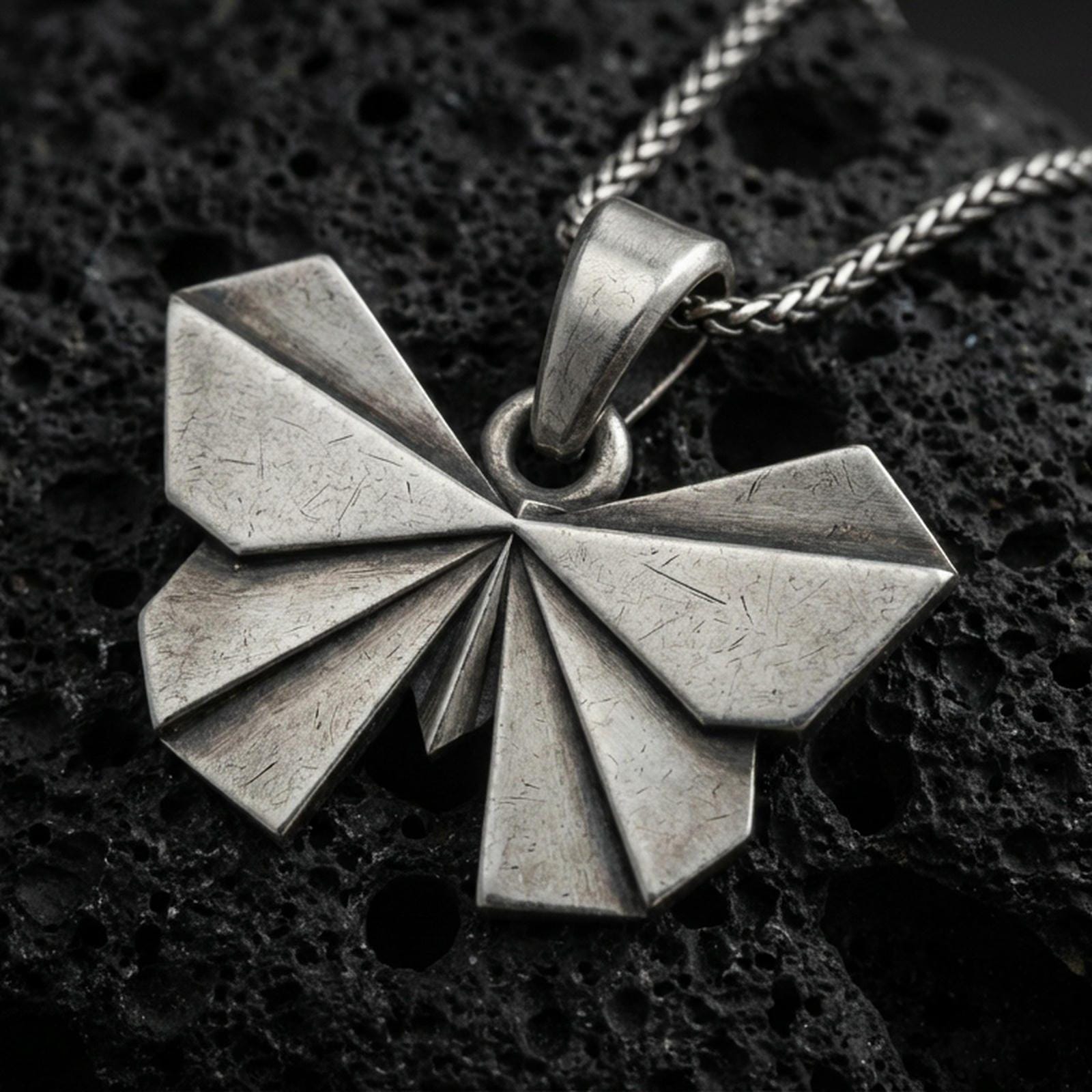 Sterling silver origami butterfly pendant necklace with an oxidized finish resting on textured volcanic rock, captured in a close-up premium studio composition.