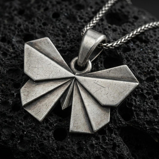Sterling silver origami butterfly pendant necklace with an oxidized finish resting on textured volcanic rock, captured in a close-up premium studio composition.