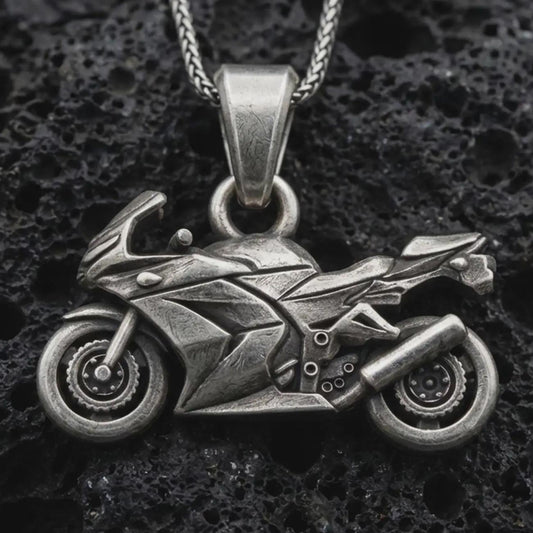 Sterling silver sportbike motorcycle pendant necklace with an oxidized finish resting on textured volcanic rock, captured in a close-up premium studio composition.