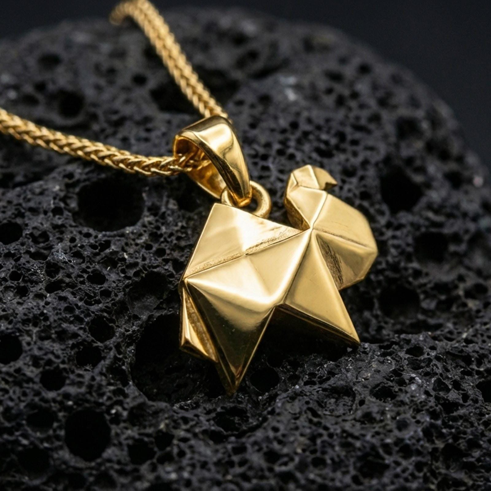 Gold plated origami camel pendant necklace presented on porous volcanic rock, highlighting the angular desert animal silhouette in a luxurious close-up jewelry image.
