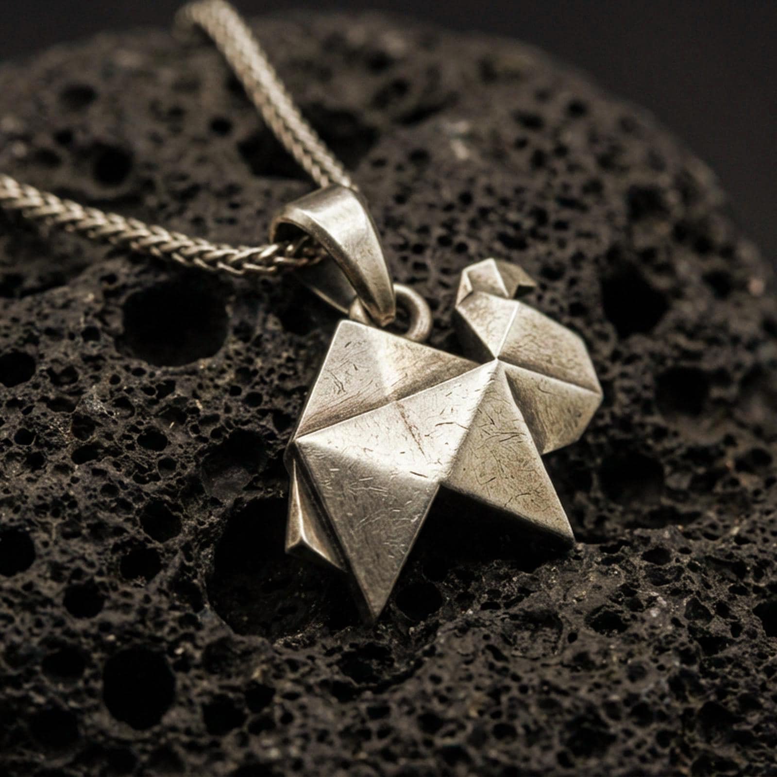 Bronze origami camel pendant necklace with an oxidized finish resting on textured volcanic rock, captured in a close-up premium studio composition.