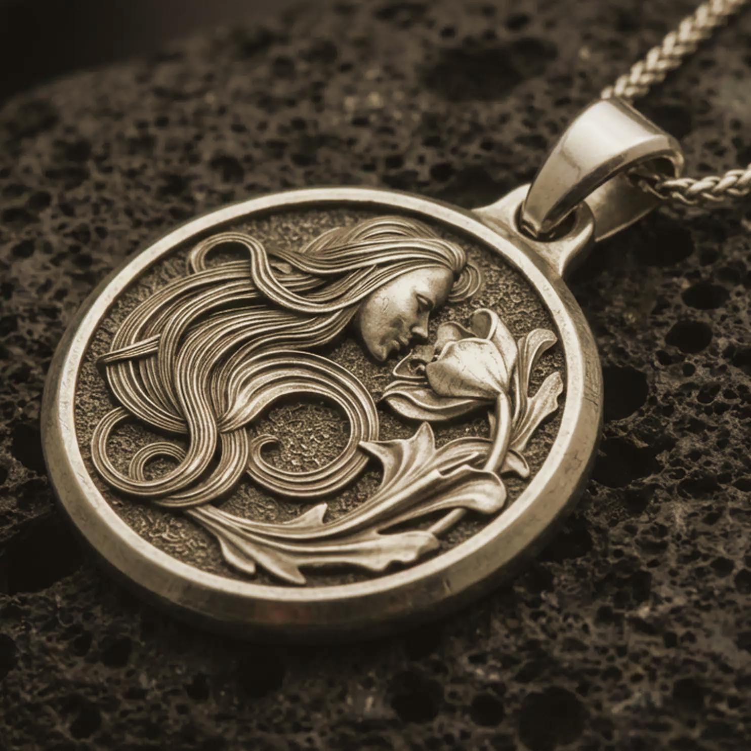 Bronze Art Nouveau woman pendant necklace with an oxidized finish resting on textured volcanic rock, captured in a close-up premium studio composition.