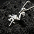 Load image into Gallery viewer, Polished silver origami flamingo pendant necklace displayed on black volcanic rock, shown in a refined macro product shot with crisp folded geometric detail.
