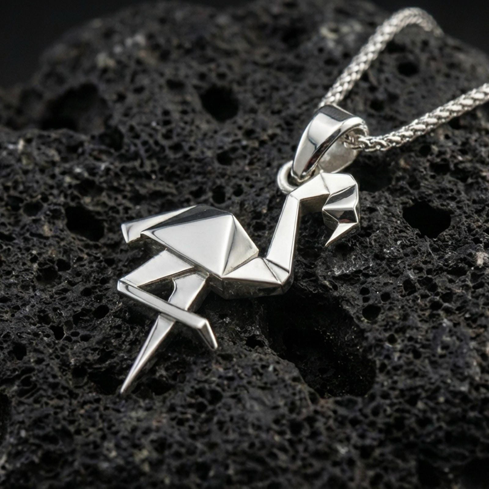 Polished silver origami flamingo pendant necklace displayed on black volcanic rock, shown in a refined macro product shot with crisp folded geometric detail.