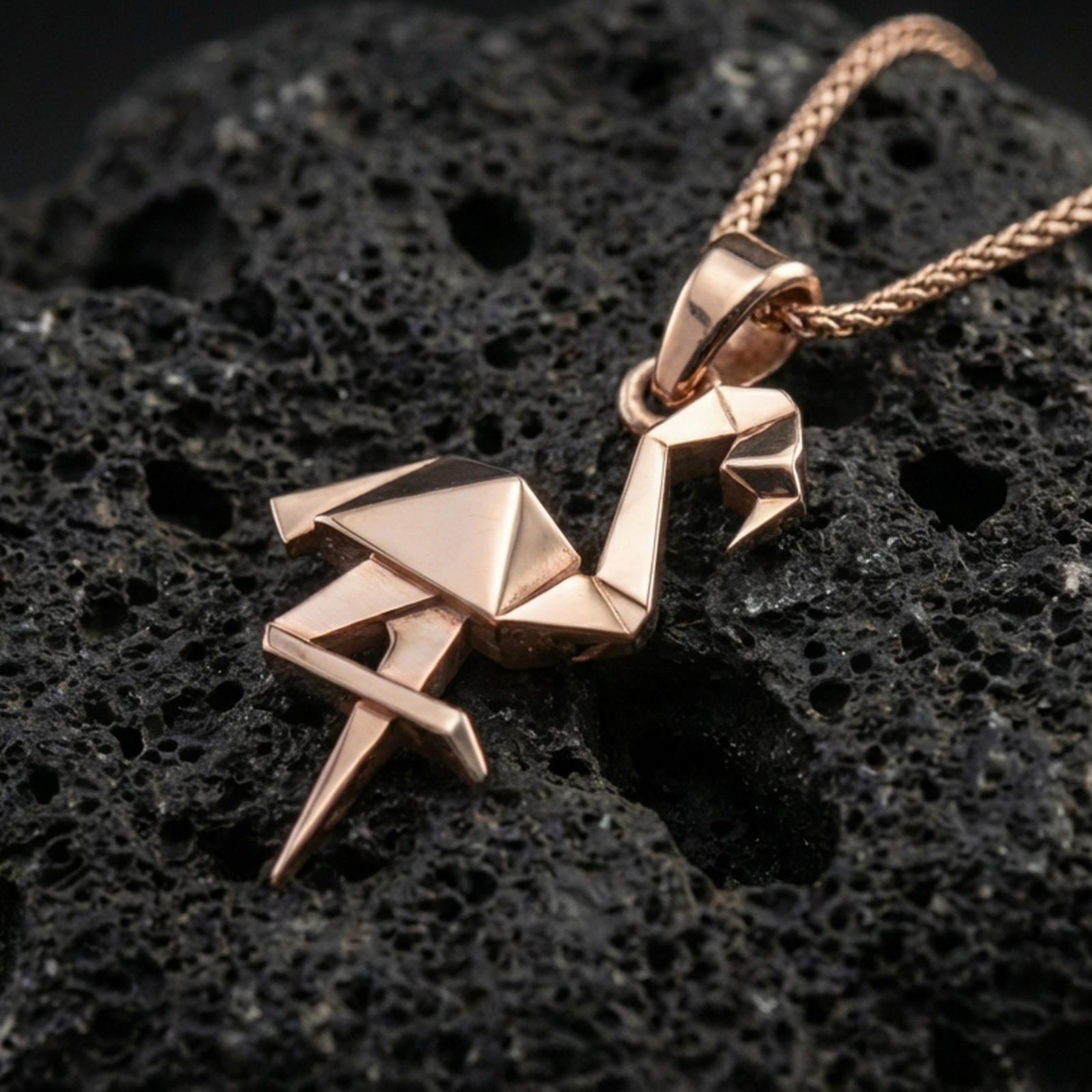 Rose gold plated origami flamingo pendant necklace on dark volcanic rock, photographed in a detailed premium studio macro view.