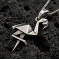 Load image into Gallery viewer, Sterling silver origami flamingo pendant necklace with an oxidized finish resting on textured volcanic rock, captured in a close-up premium studio composition.
