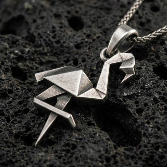 Sterling silver origami flamingo pendant necklace with an oxidized finish resting on textured volcanic rock, captured in a close-up premium studio composition.