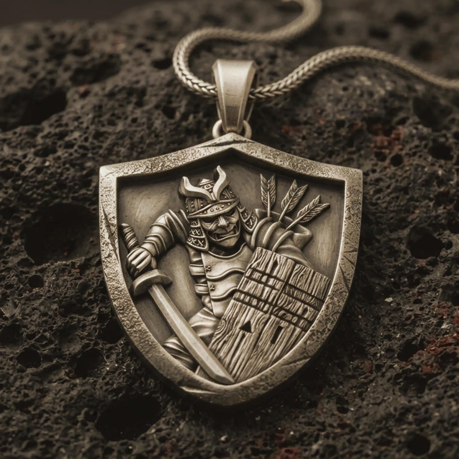 Bronze samurai shield pendant necklace with an oxidized finish resting on textured volcanic rock, captured in a close-up premium studio composition.