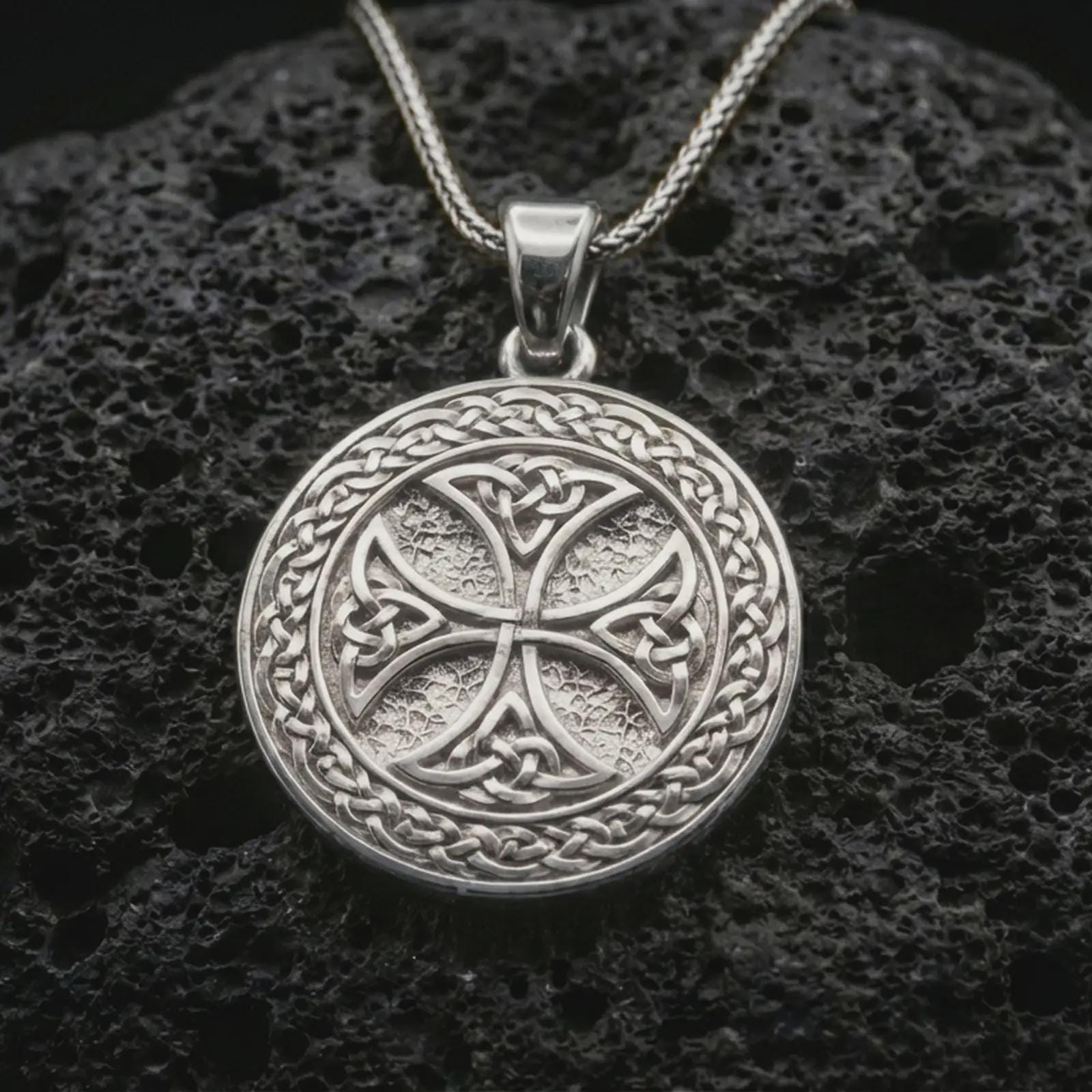 Polished silver Celtic knot medallion necklace displayed on black volcanic rock, shown in a refined macro product shot with intricate Gaelic weave and circular symbolic relief.