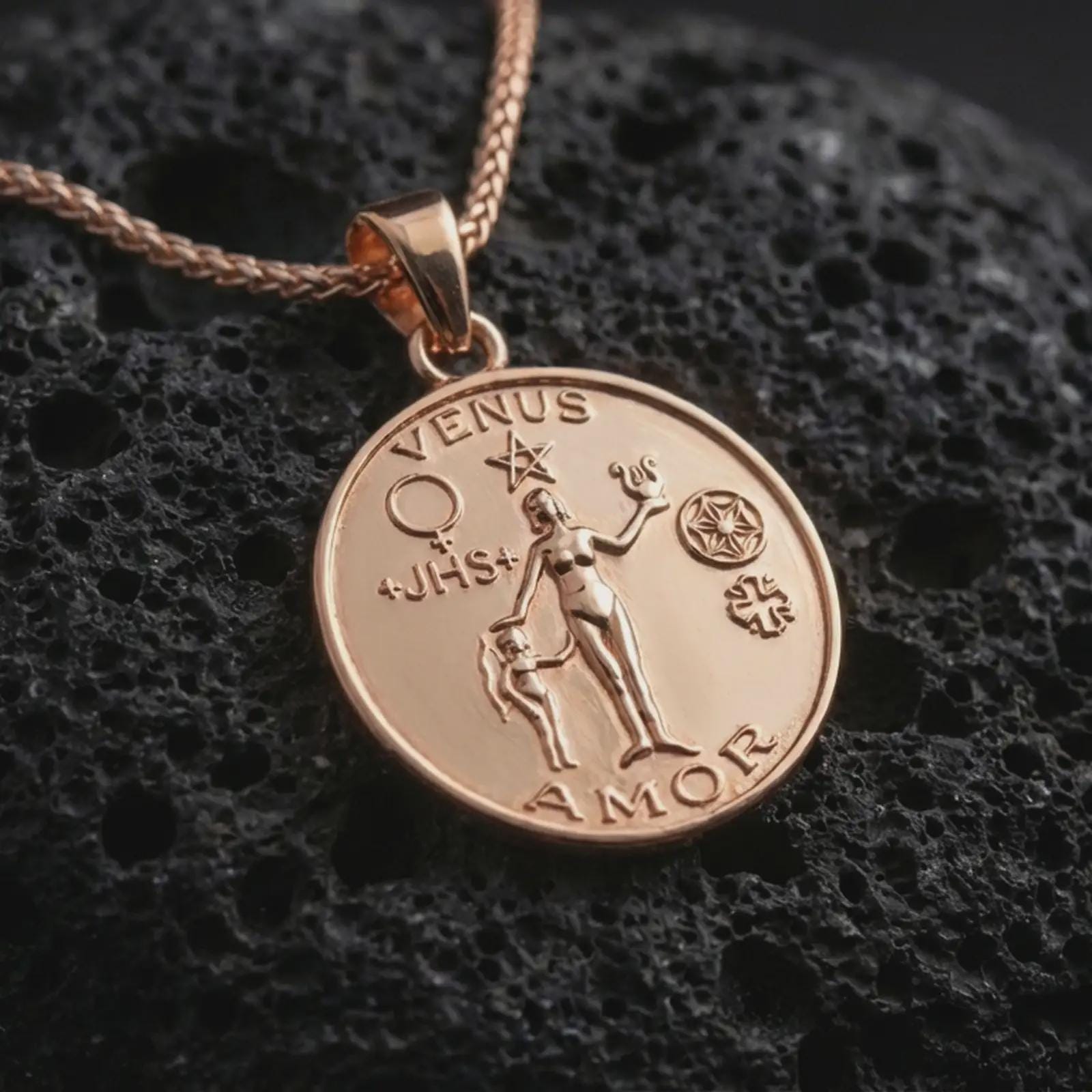 Rose gold plated Venus Amor pendant necklace on dark volcanic rock, photographed in a detailed premium studio macro view.