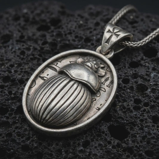 Sterling silver Egyptian scarab pendant necklace with an oxidized finish resting on textured volcanic rock, captured in a close-up premium studio composition.