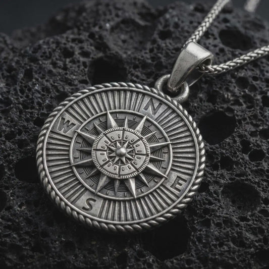 Sterling silver steampunk compass pendant necklace with an oxidized finish resting on textured volcanic rock, captured in a close-up premium studio composition.