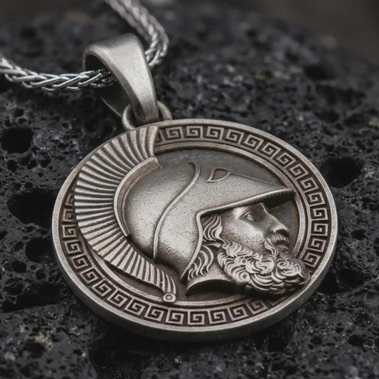 Sterling silver Spartan helmet pendant necklace with an oxidized finish resting on textured volcanic rock, captured in a close-up premium studio composition.