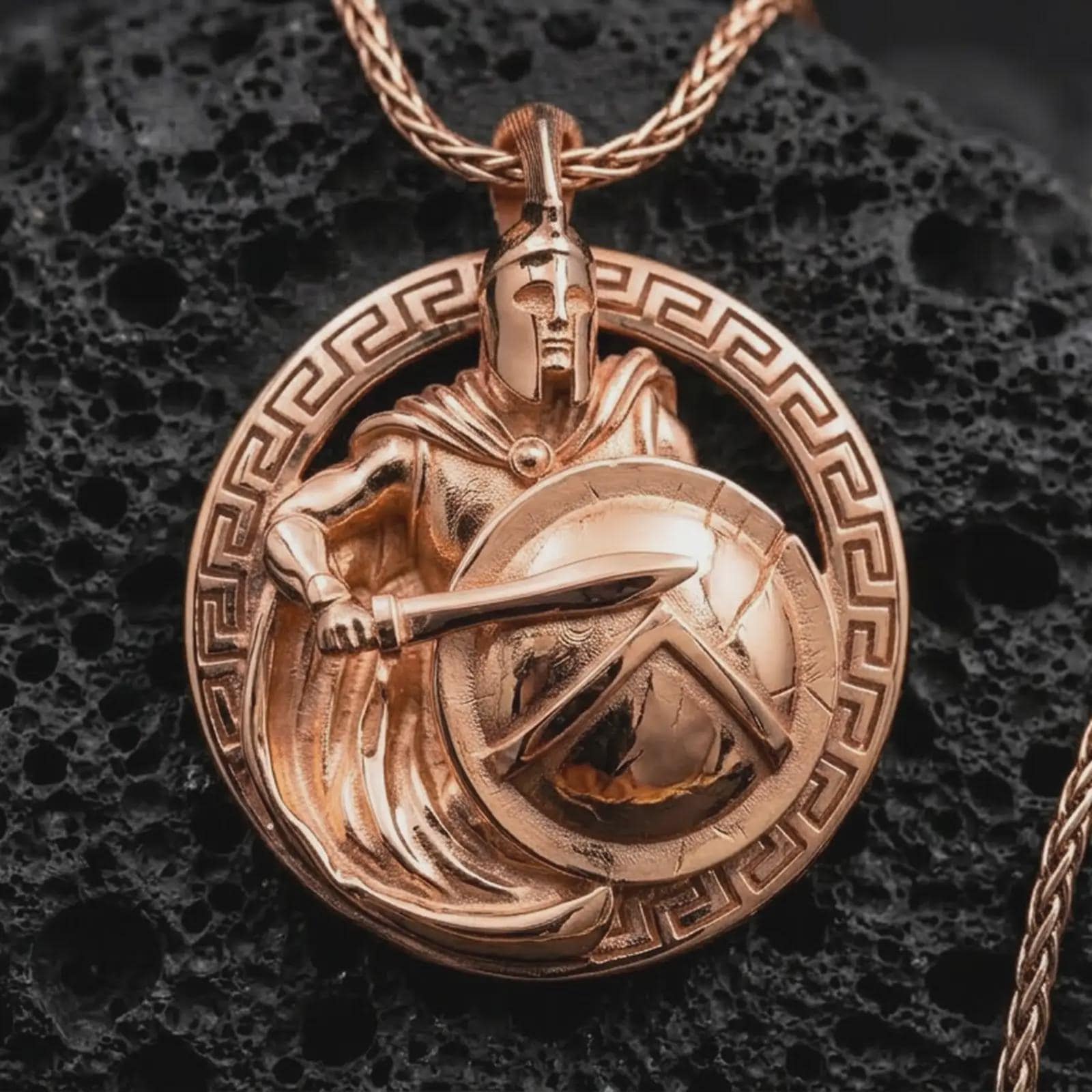 Rose gold plated Spartan warrior pendant necklace on dark volcanic rock, photographed in a detailed premium studio macro view.
