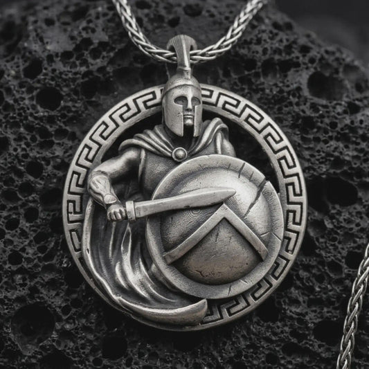 Sterling silver Spartan warrior pendant necklace with an oxidized finish resting on textured volcanic rock, captured in a close-up premium studio composition.