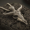Load image into Gallery viewer, Bronze Baphomet skull pendant necklace with an oxidized finish resting on textured volcanic rock, captured in a close-up premium studio composition.
