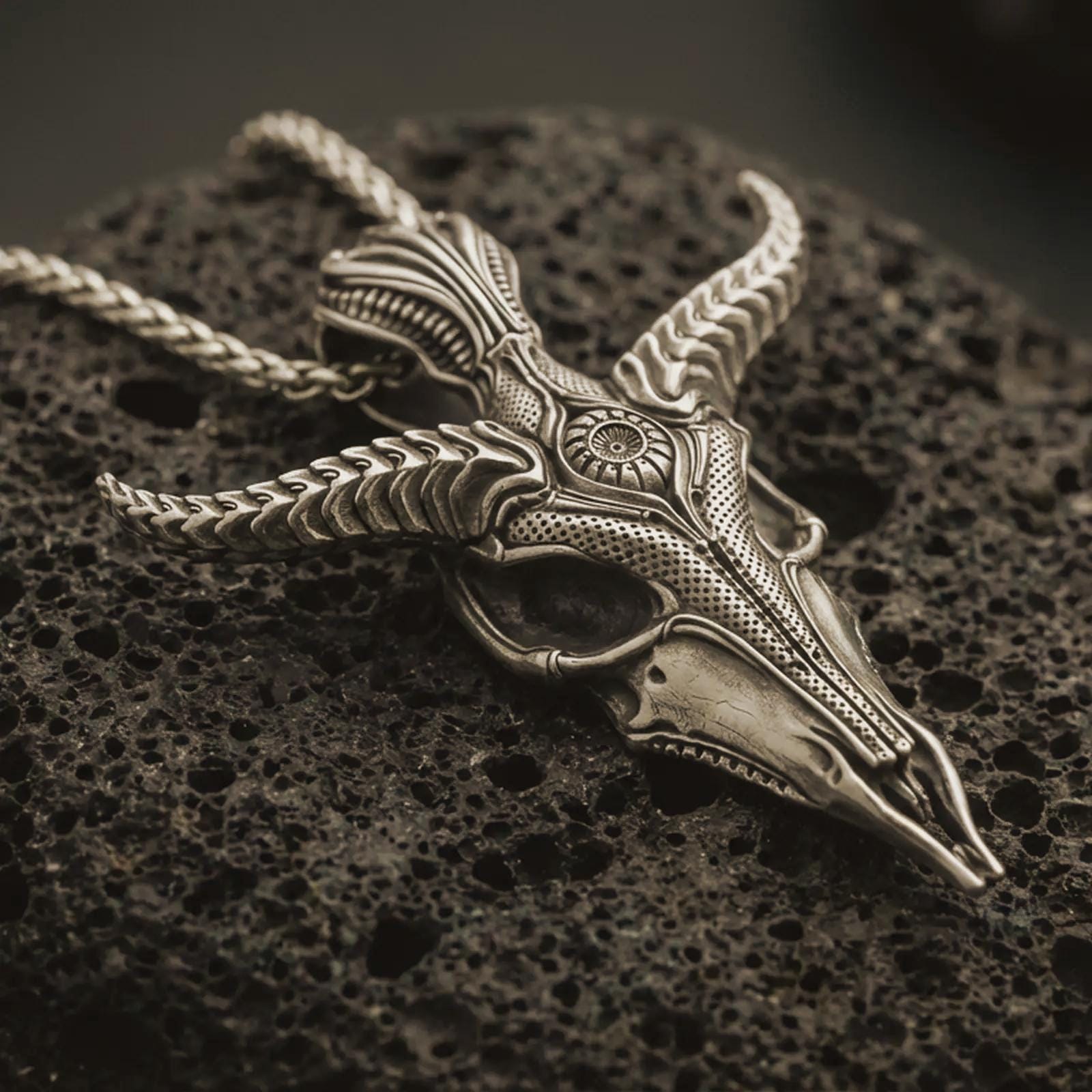 Bronze Baphomet skull pendant necklace with an oxidized finish resting on textured volcanic rock, captured in a close-up premium studio composition.