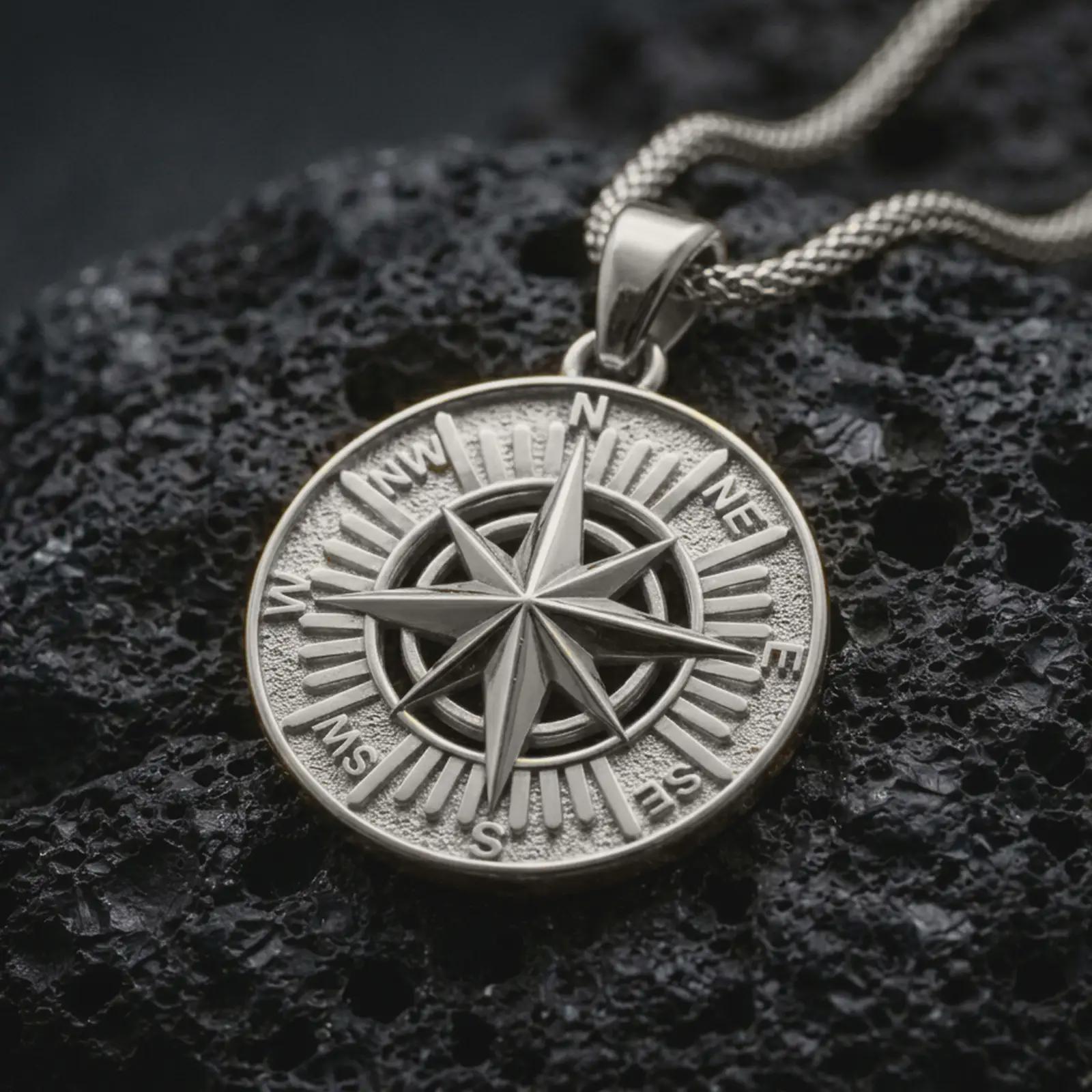 Polished silver compass rose pendant necklace displayed on black volcanic rock, shown in a refined macro product shot with cardinal direction letters and sharp navigational star detail.