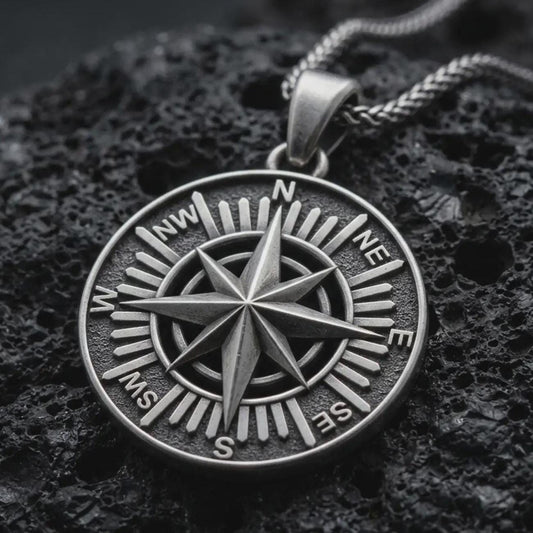 Sterling silver compass rose pendant necklace with an oxidized finish resting on textured volcanic rock, captured in a close-up premium studio composition.