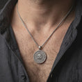 Load image into Gallery viewer, Oxidized cursed Aztec coin pendant necklace worn on the neck, styled on a human model in a dark lifestyle portrait with an open shirt and bold masculine presentation.
