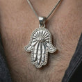 Load image into Gallery viewer, Polished silver Hamsa hand pendant necklace worn on the neck, shown against the chest in a clean and meaningful everyday wear composition.
