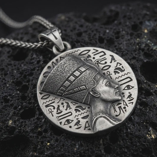 Sterling silver Nefertiti medallion pendant necklace with an oxidized finish resting on textured volcanic rock, captured in a close-up premium studio composition.