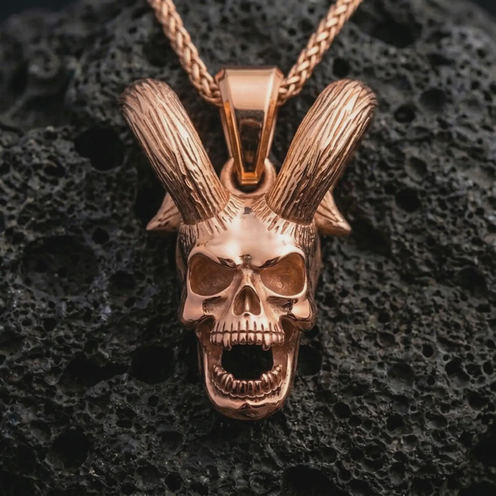 Rose gold plated rabbit skull pendant necklace on dark volcanic rock, photographed in a detailed premium studio macro view.