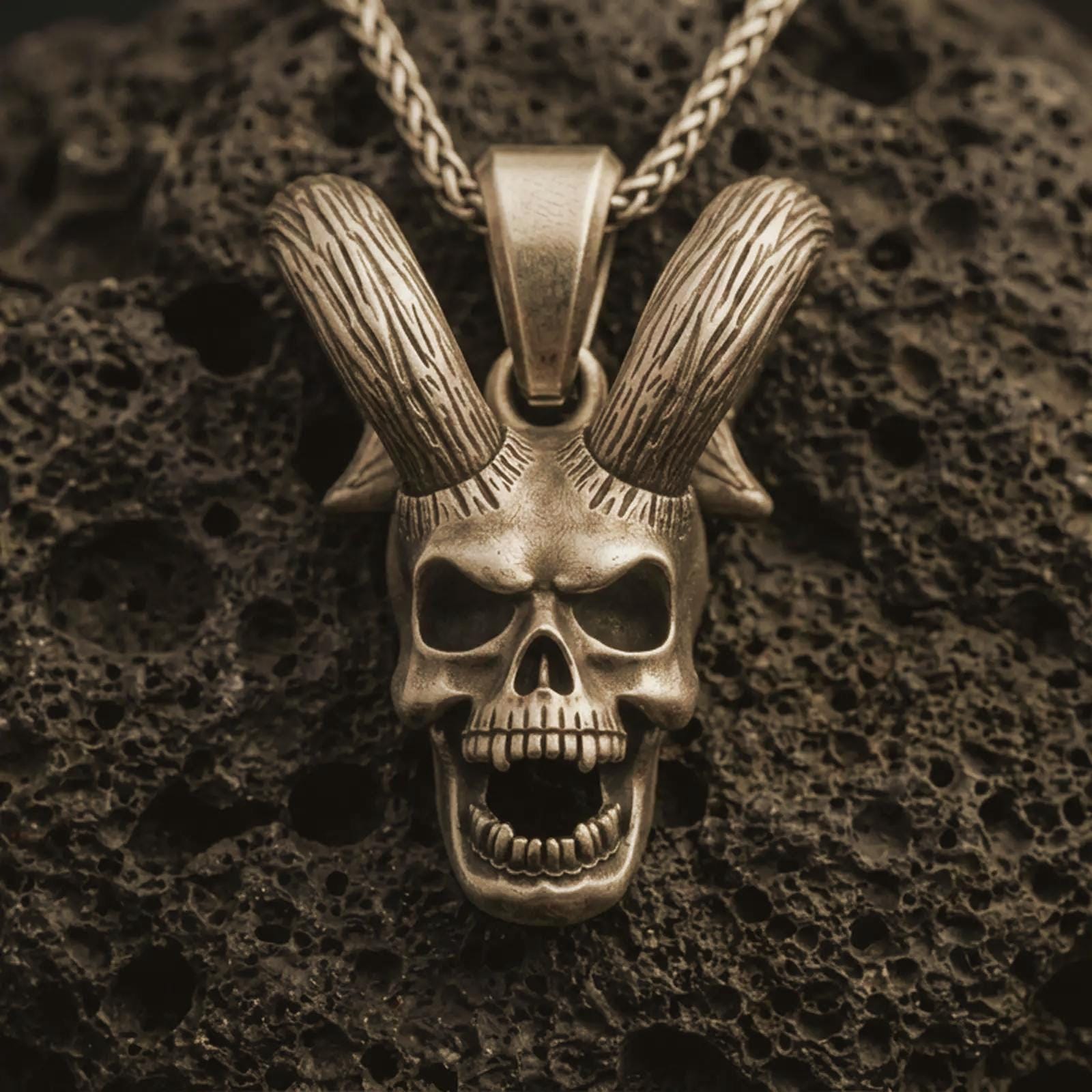 Bronze rabbit skull pendant necklace with an oxidized finish resting on textured volcanic rock, captured in a close-up premium studio composition.