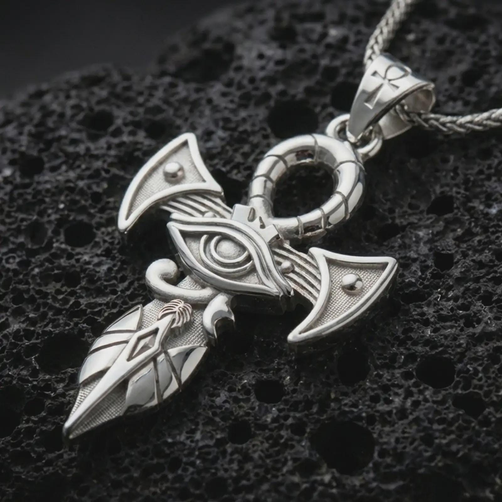 Polished silver Eye of Horus ankh pendant necklace displayed on black volcanic rock, shown in a refined macro product shot with sacred eye detail, geometric blades, and ankh-inspired top ring.
