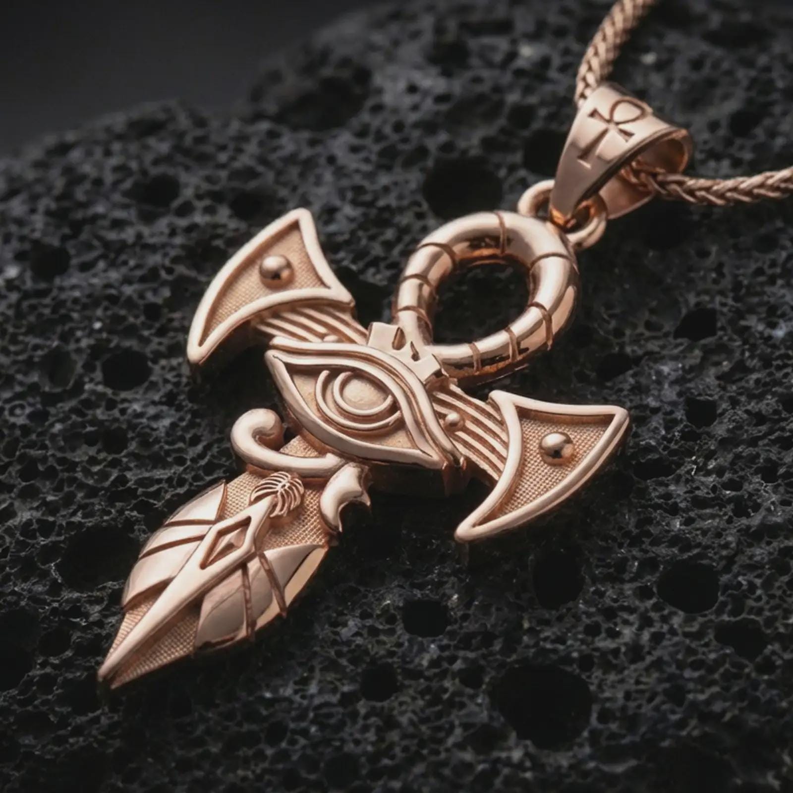 Rose gold plated Eye of Horus ankh pendant necklace on dark volcanic rock, photographed in a detailed premium studio macro view.