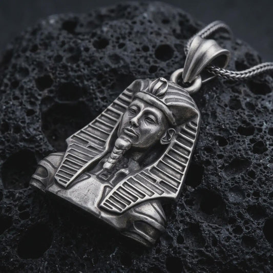 Sterling silver Tutankhamun pendant necklace with an oxidized finish resting on textured volcanic rock, captured in a close-up premium studio composition.