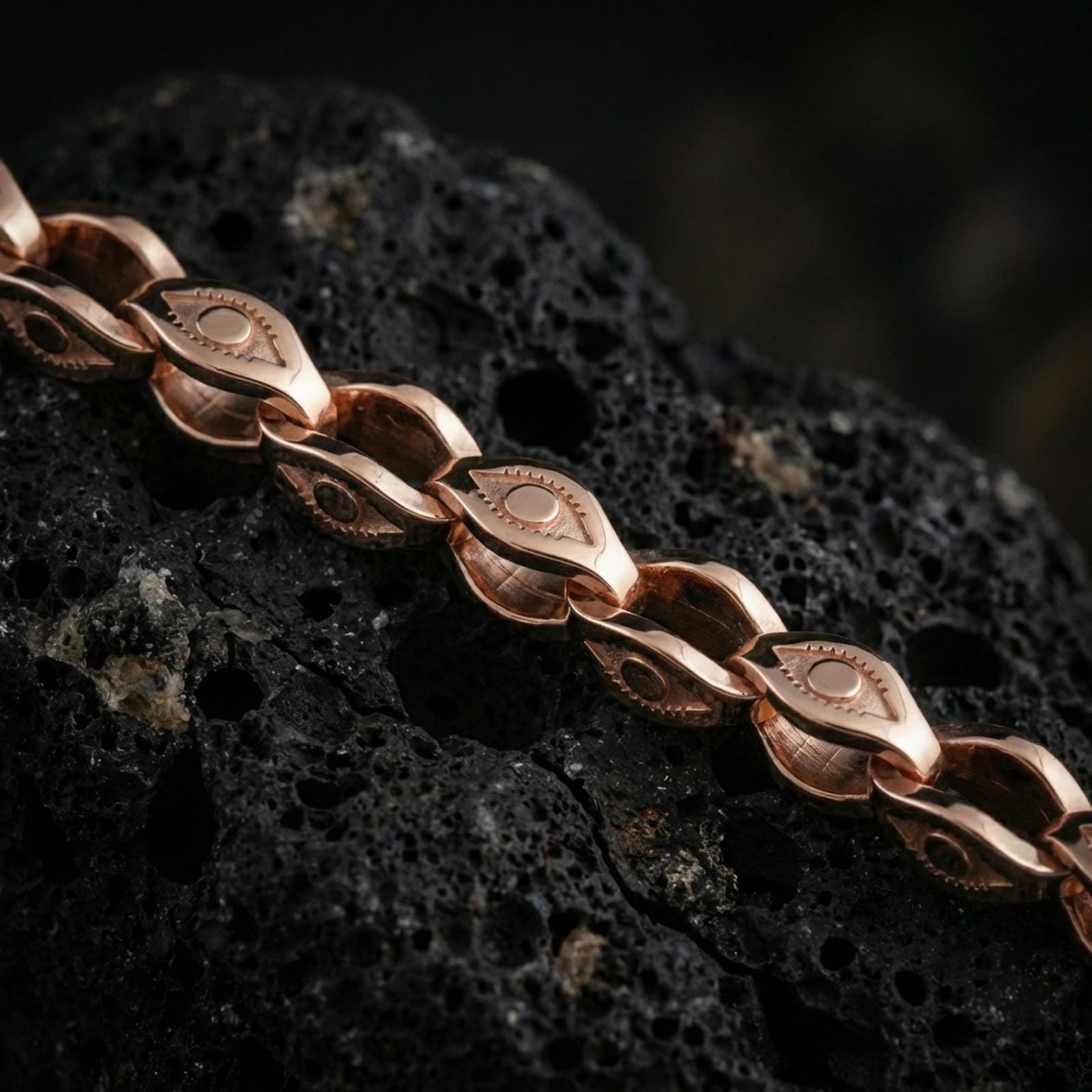 Rose gold plated evil eye link chain necklace on dark volcanic rock, photographed in a detailed premium studio macro view.