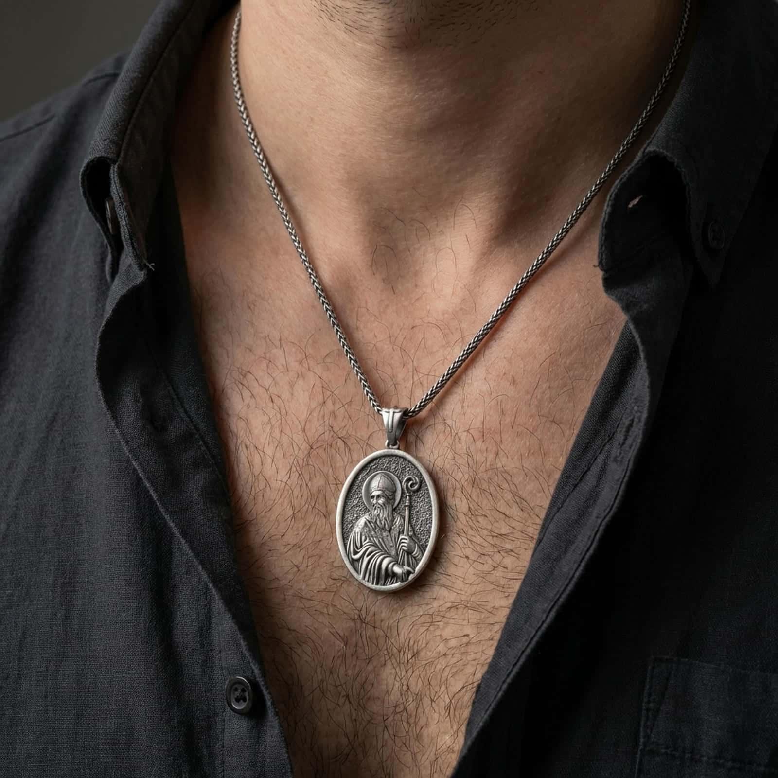 Oxidized Saint Patrick pendant necklace worn on the neck, styled in a dark lifestyle portrait with an open shirt and masculine presentation.