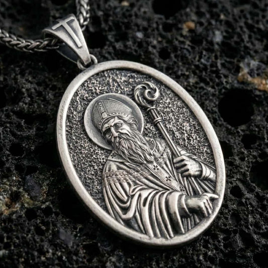 Sterling silver Saint Patrick pendant necklace with an oxidized finish resting on textured volcanic rock, captured in a close-up premium studio composition.