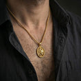Load image into Gallery viewer, Gold plated Saint Sebastian pendant necklace worn on the neck, captured on a human model in a premium dark-toned lifestyle frame.
