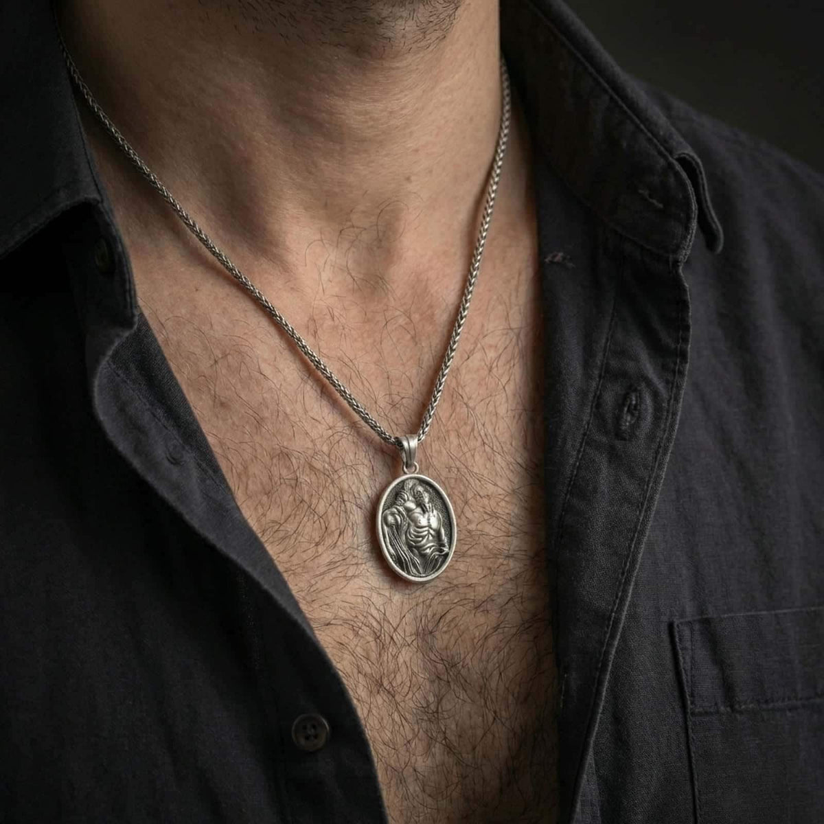 Oxidized Saint Sebastian pendant necklace worn on the neck, styled in a dark lifestyle portrait with an open shirt and masculine presentation.