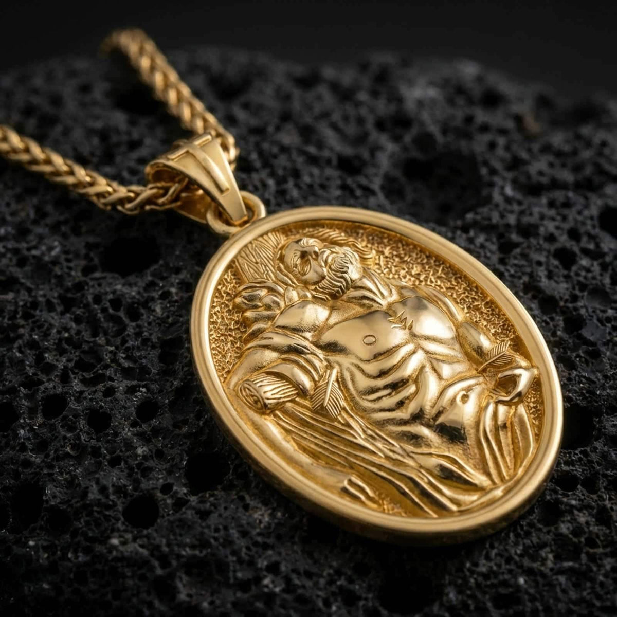 Gold plated Saint Sebastian pendant necklace presented on porous volcanic rock, highlighting the oval medallion form and sacred devotional design in a luxurious close-up jewelry image.