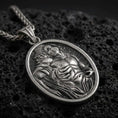 Load image into Gallery viewer, Sterling silver Saint Sebastian pendant necklace with an oxidized finish resting on textured volcanic rock, captured in a close-up premium studio composition.

