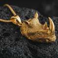 Load image into Gallery viewer, Gold plated rhinoceros head pendant necklace presented on porous volcanic rock, highlighting the powerful animal head silhouette in a luxurious close-up jewelry image.
