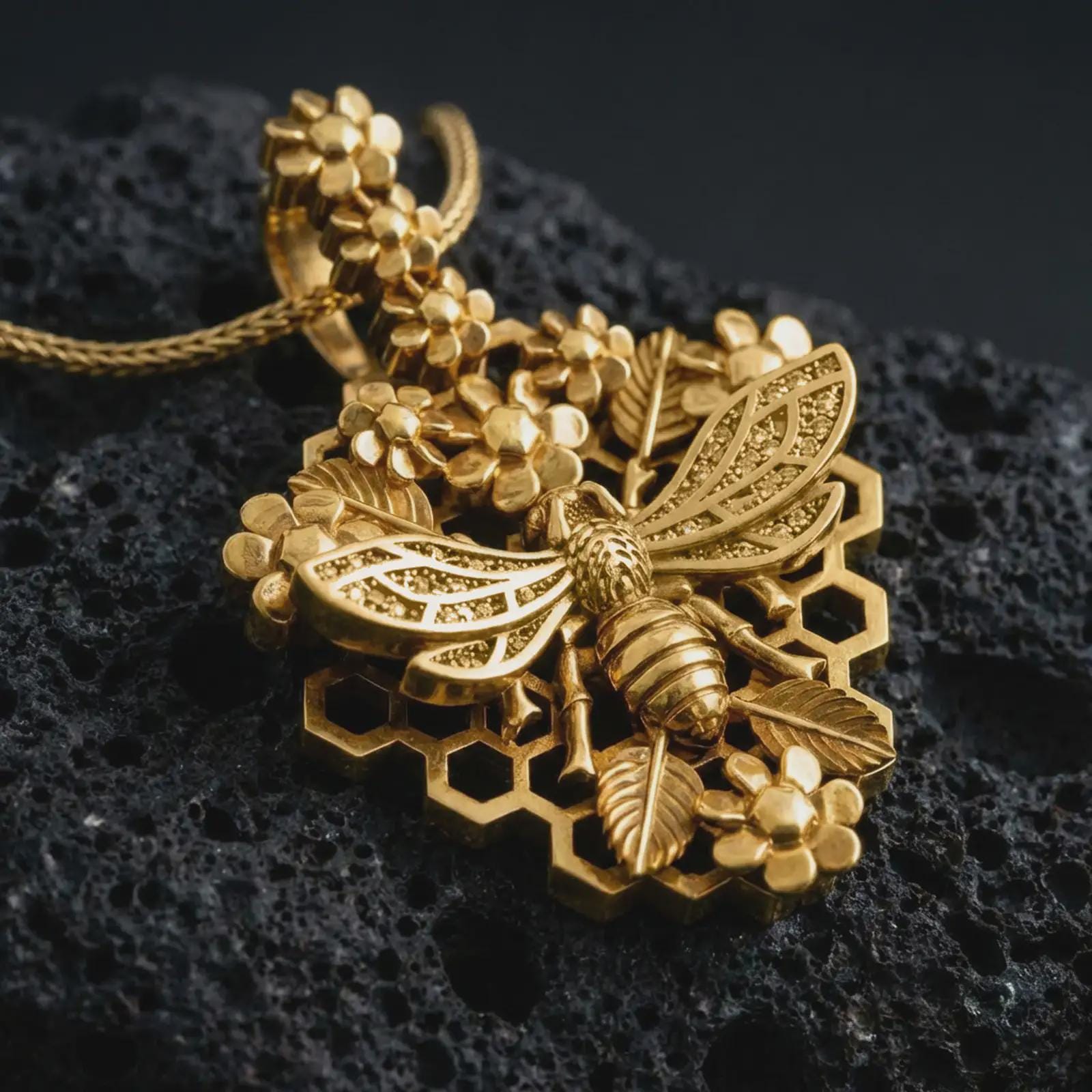 Gold plated floral bee pendant necklace presented on porous volcanic rock, highlighting the nature-inspired honeybee and blossom motif in a luxurious close-up jewelry image.