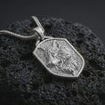 Load image into Gallery viewer, Polished silver wolf shield pendant necklace displayed on black volcanic rock, shown in a refined macro product shot with flowing fur detail, wolf face relief, and geometric shield frame.
