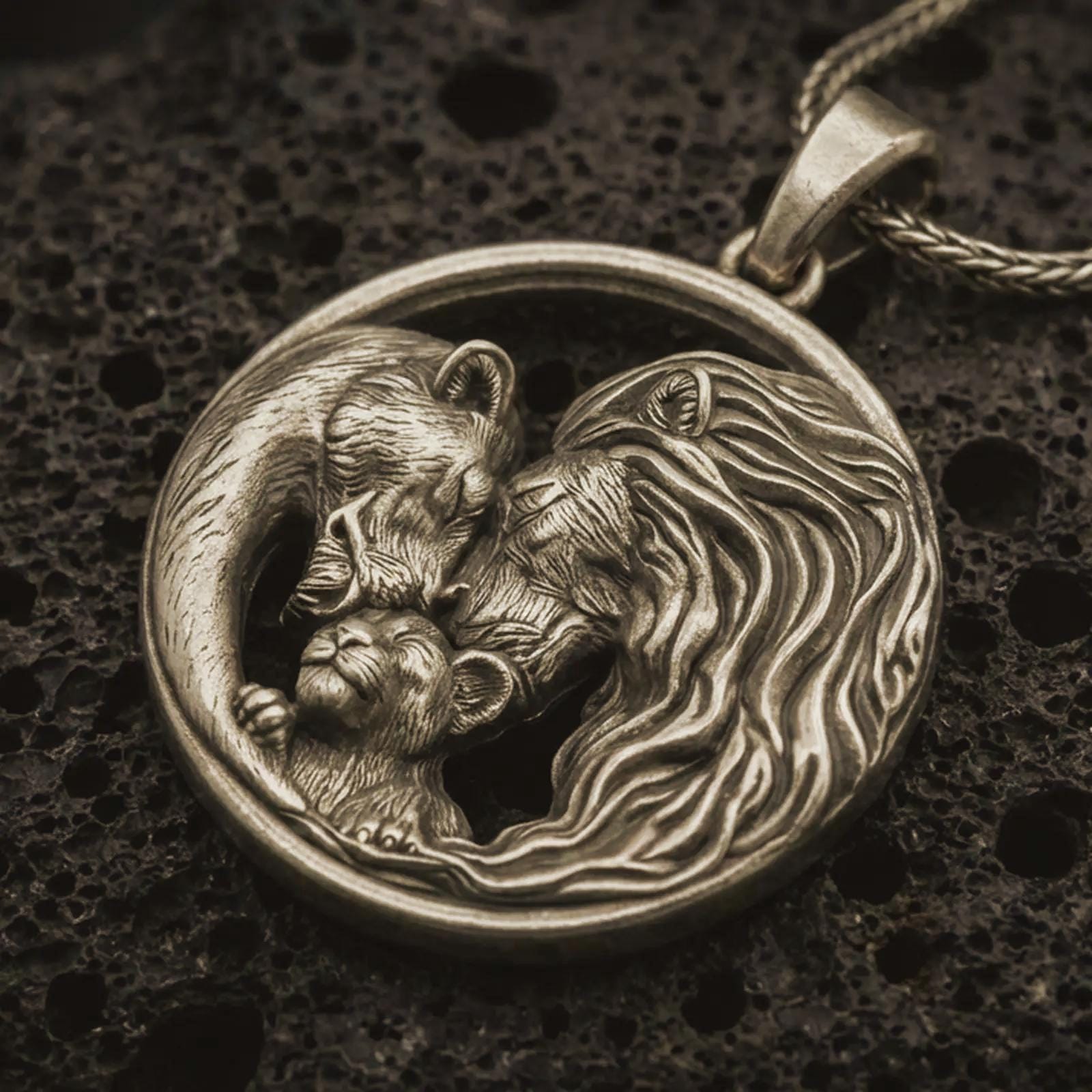 Bronze lion and bear family pendant necklace with an oxidized finish resting on textured volcanic rock, captured in a close-up premium studio composition.