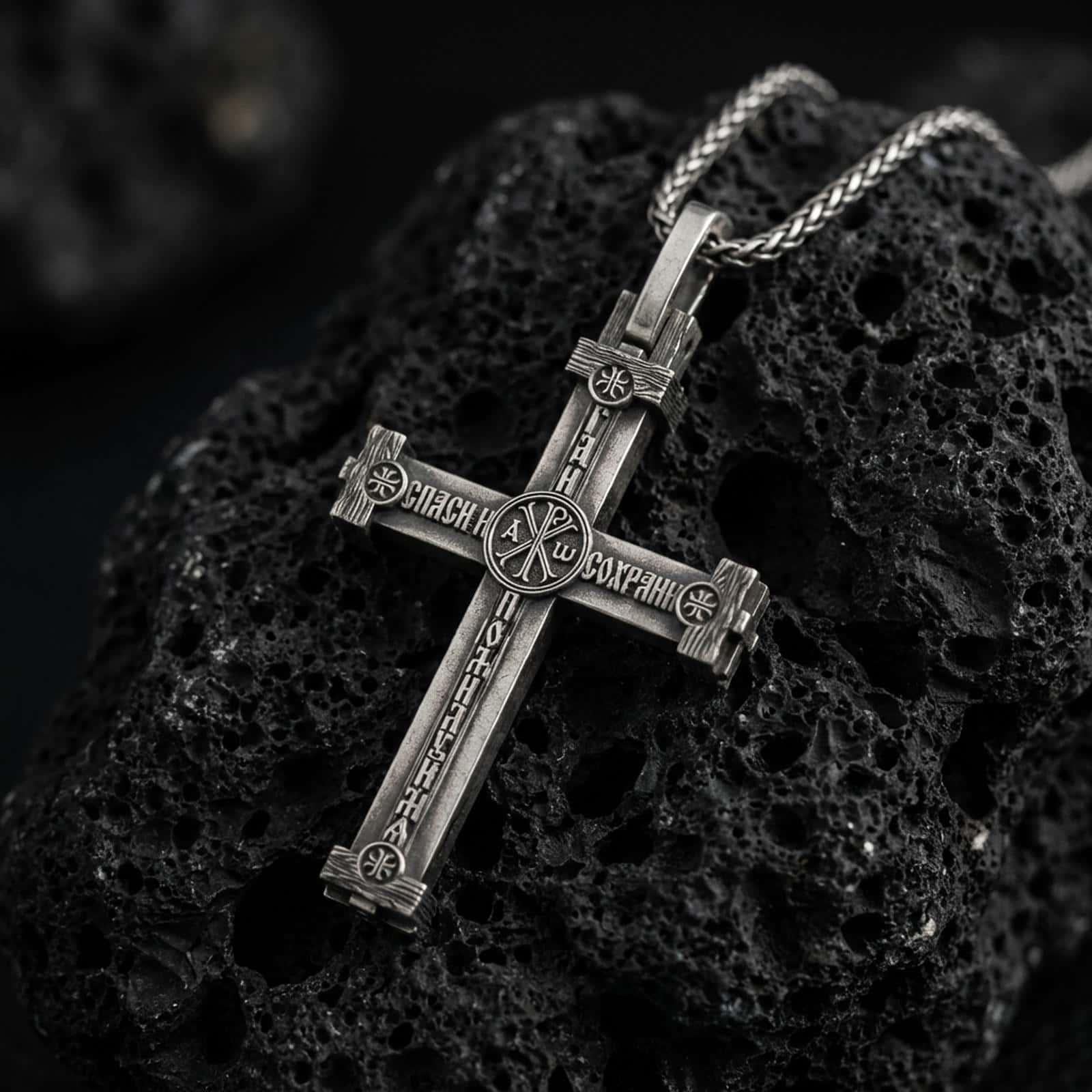 Sterling silver Orthodox cross pendant necklace backside with an oxidized finish resting on textured volcanic rock, captured in a close-up premium studio composition.