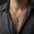 Load image into Gallery viewer, Oxidized Orthodox cross pendant necklace worn on the neck, styled in a dark lifestyle portrait with an open shirt and masculine presentation.
