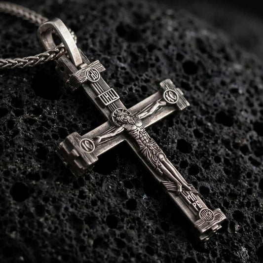 Sterling silver Orthodox cross pendant necklace with an oxidized finish resting on textured volcanic rock, captured in a close-up premium studio composition.