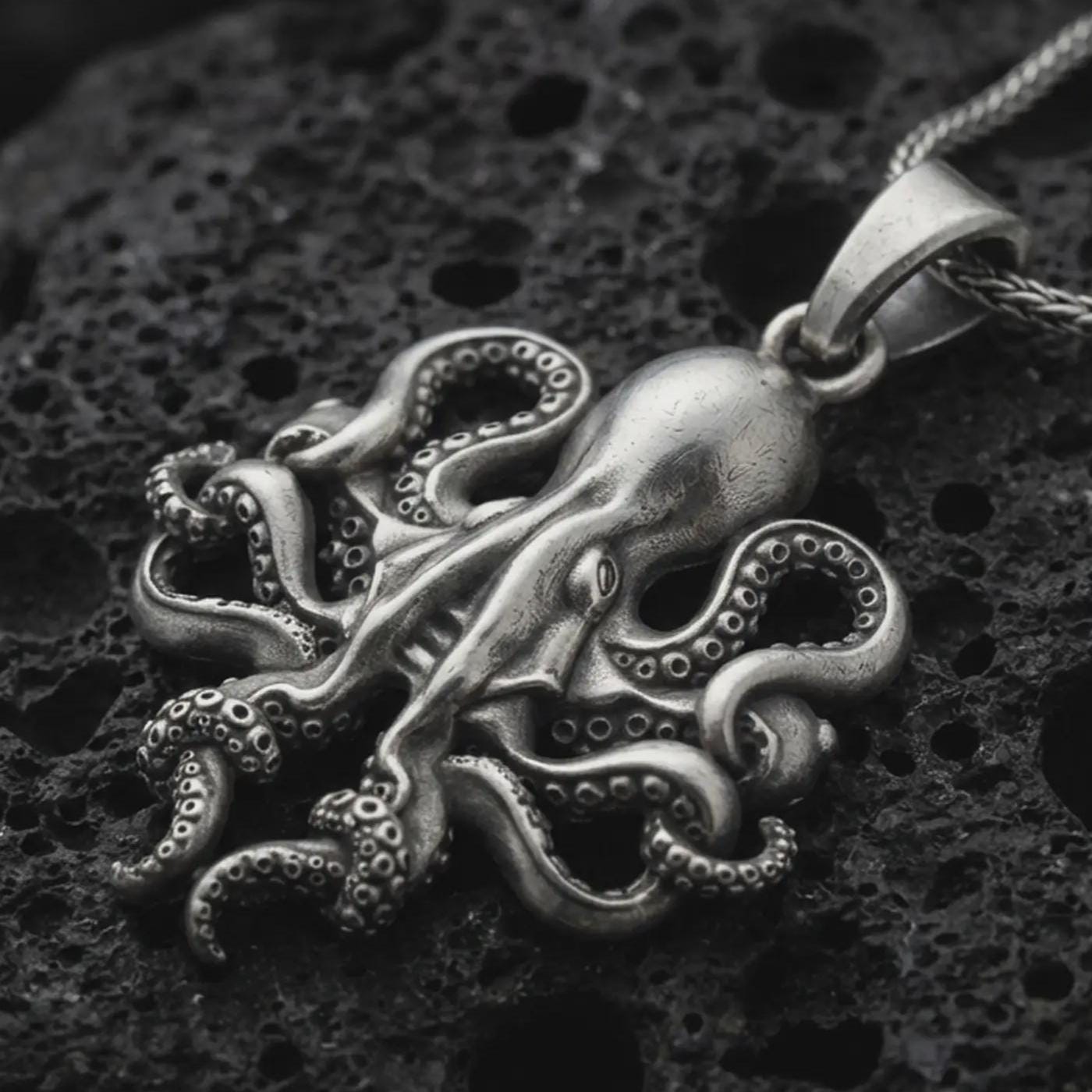 Sterling silver octopus pendant necklace with an oxidized finish resting on textured volcanic rock, captured in a close-up premium studio composition.