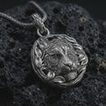 Load image into Gallery viewer, A tiger pendant on black volcanic stone with oxidized contrast highlighting the leaf wreath frame and engraved stripes.
